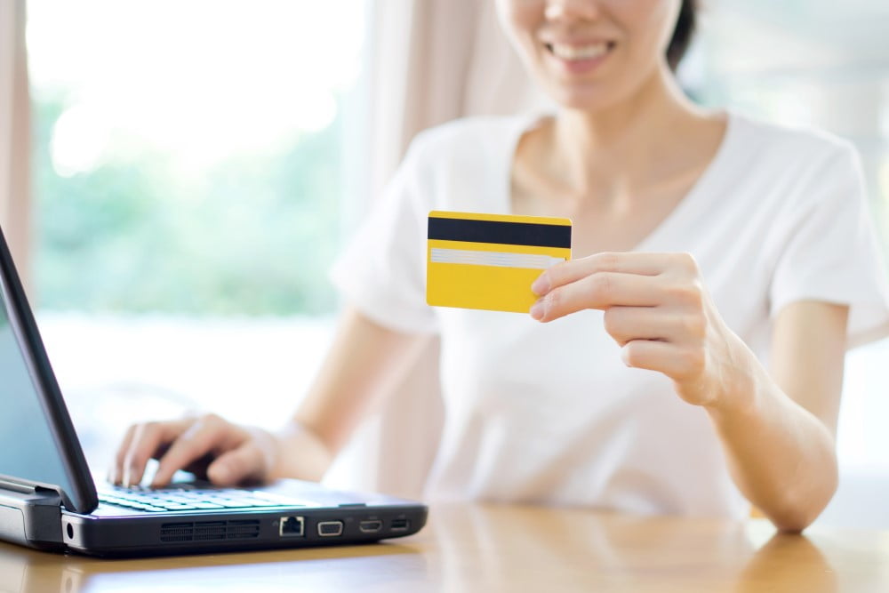 Smilende kvinde med laptop og kreditkort